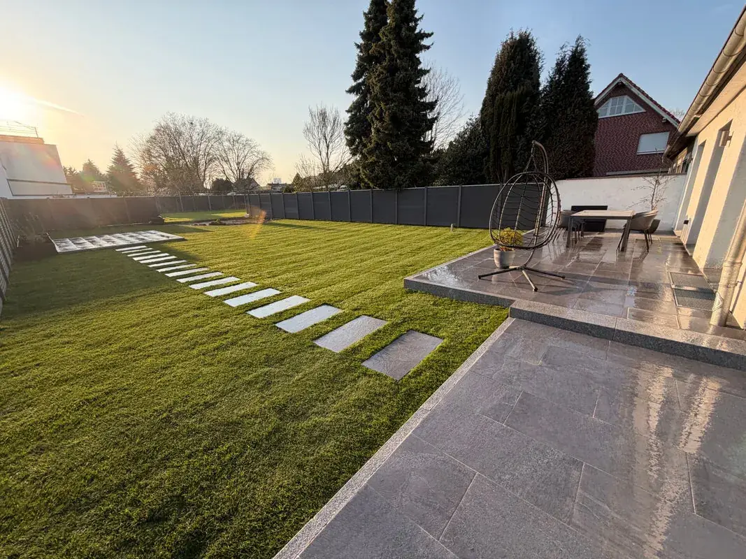 Fertiggestellter Garten mit Rollrasen, Stegplatten, grauer Terrasse und Sichtschutzzaun im Abendlicht