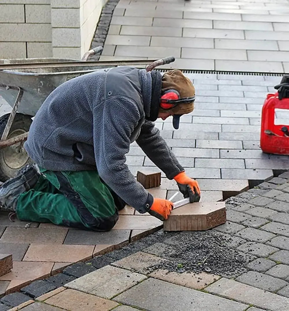Mitarbeiter kniet und vermisst einen Pflasterstein beim Pflastern